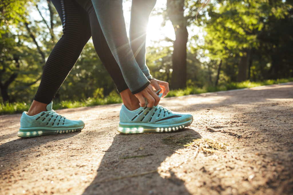 Une personne attachant ses chaussures de sport dans un chemin forestier ensoleillé, prête à pratiquer une activité physique.