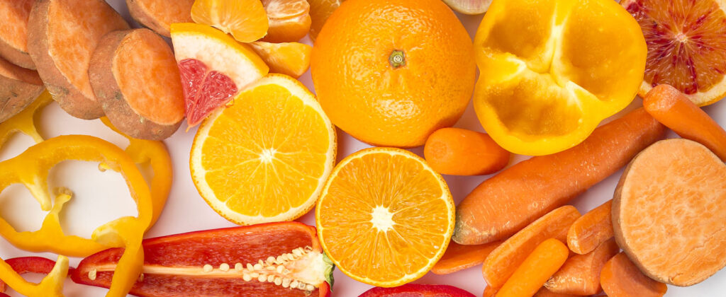 Un assortiment de fruits et légumes orange riches en bêta-carotène, tels que des oranges, carottes, poivrons jaunes, patates douces et pamplemousses.