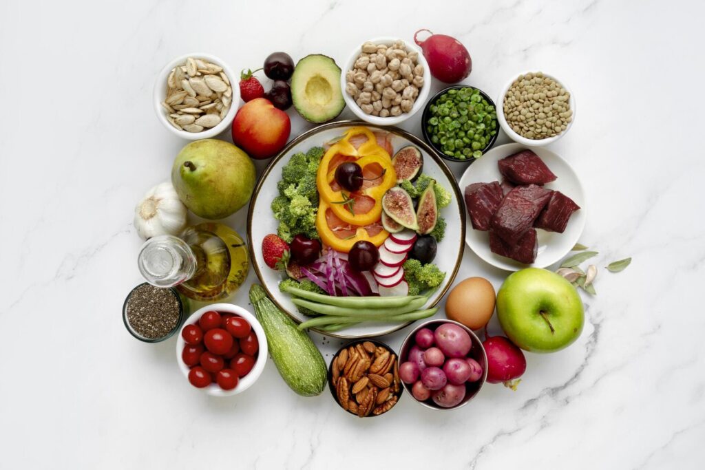 Un assortiment équilibré d'aliments sains comprenant des légumes, fruits, protéines, légumineuses, noix et huiles, disposés harmonieusement sur une table en marbre.