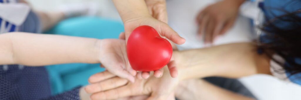 Des mains se transmettant un cœur rouge en symbole de soin et de solidarité.