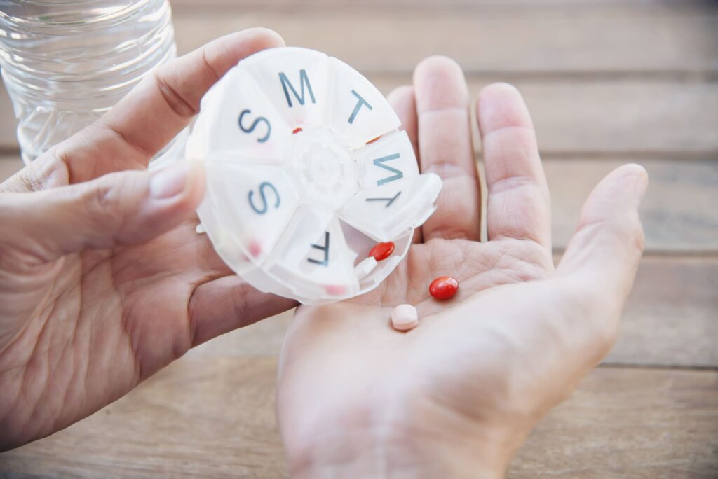 Gros plan sur une main tenant un pilulier rond, avec des médicaments pour différents jours de la semaine.