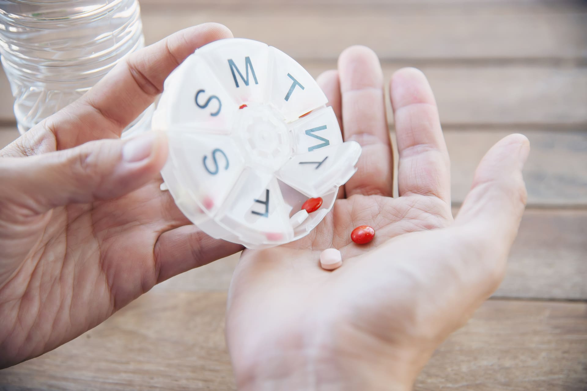 Gros plan sur une main tenant un pilulier rond, avec des médicaments pour différents jours de la semaine.